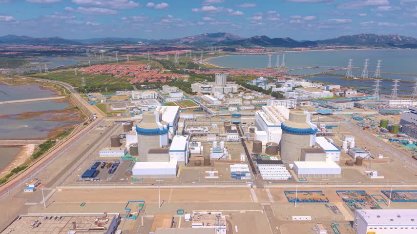 Aerial shot of a large operational nuclear power facility with surrounding water bodies and distant mountains.
