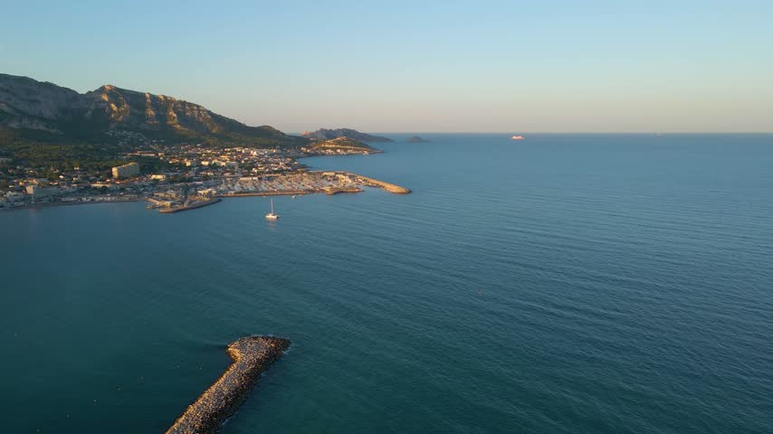 High aerial view of Marseille where gentle waves meet the shoreline and the city sits beneath the surrounding hills.