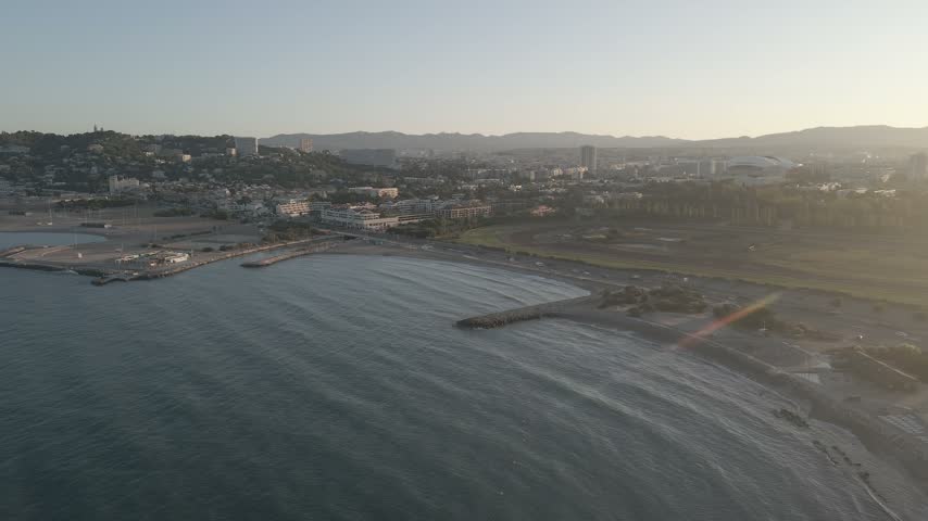 High aerial view of Marseille where gentle waves meet the shoreline and the city sits beneath the surrounding hills.