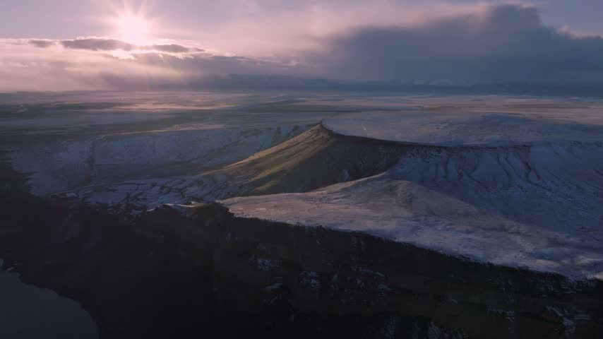 Canyon wilderness landscape featuring snow dusted plateaus winding river waters and glowing sunset light captured from an aerial perspective