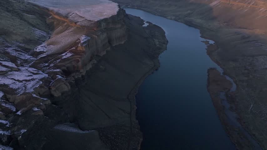 Canyon terrain featuring a winding river and snowy plateaus captured from above during twilight conditions