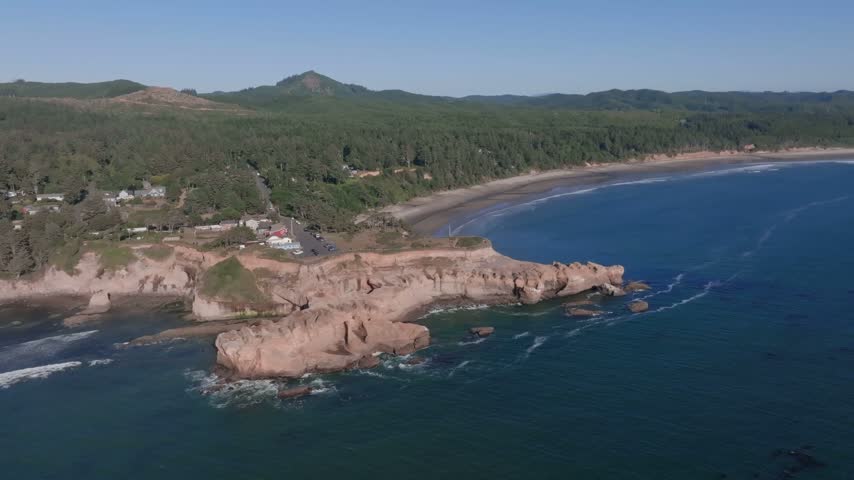 Oregon coastal landscape featuring steep cliffs meeting the blue ocean sandy shorelines and dense pine forests under clear blue skies