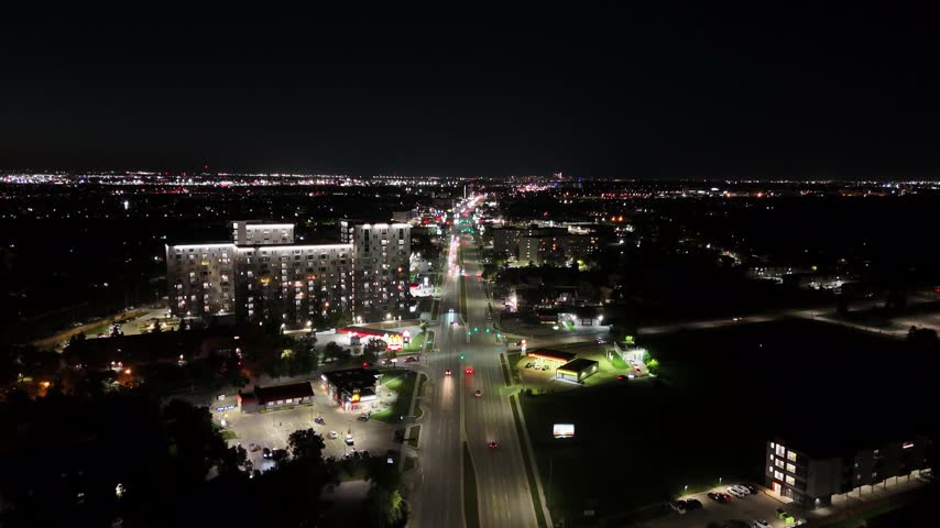 Night drone aerial flying forward north down Pembina Highway showing illuminated apartment buildings, streetlights, and traffic in South Winnipeg, Manitoba, Canada.