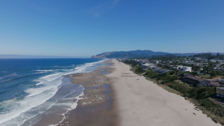 Oregon coastal landscape captured from above displaying wide sandy shores meeting blue ocean waters alongside residential properties perched on green bluffs