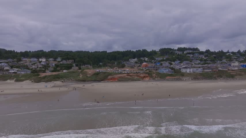 Oregon coastal town captured from an aerial perspective showcasing ocean waves sandy beaches residential housing and a thick evergreen forest landscape