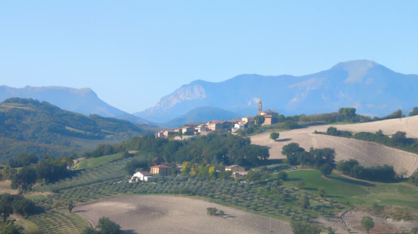 Overview of a characteristic Italian village nestled in the hills, with majestic mountains in the background