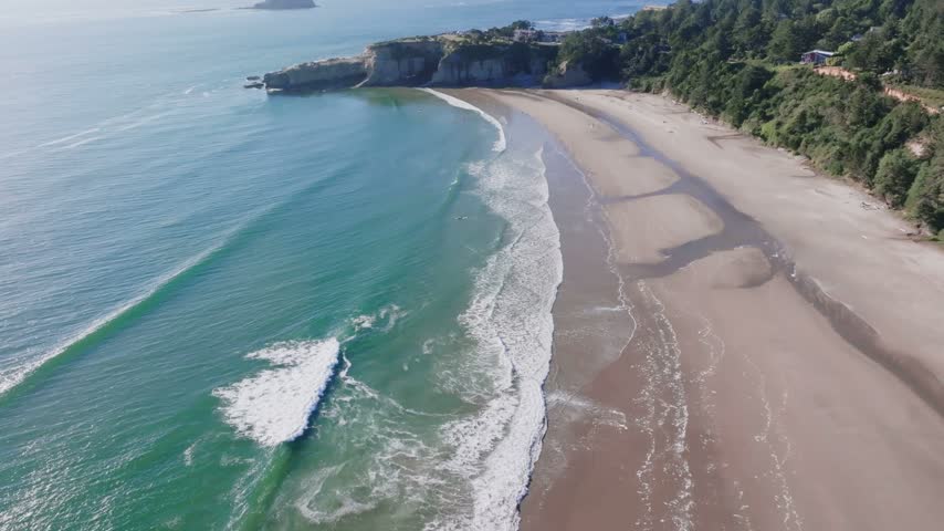 Oregon coastline featuring sandy beaches turquoise ocean waves and forested cliffs under clear daylight in aerial perspective