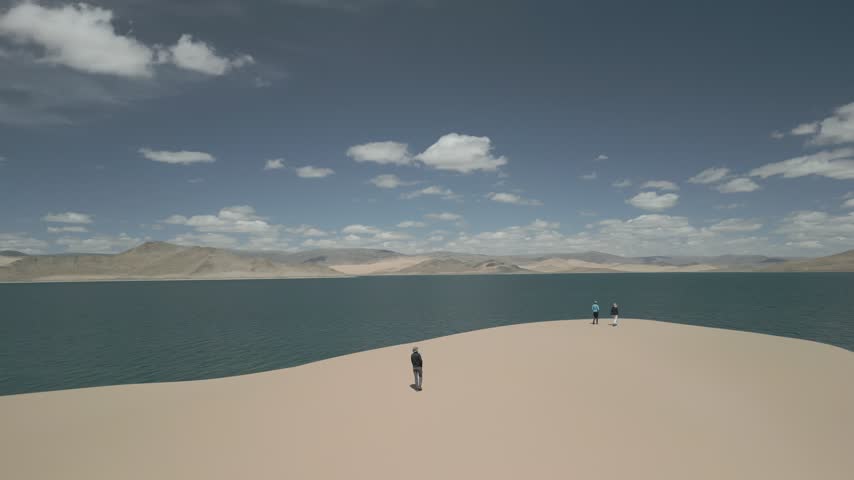 Low altitude aerial shot chasing a group of friends climbing a sand dune, flying forward over them to reveal a majestic emerald lake, flat log profile