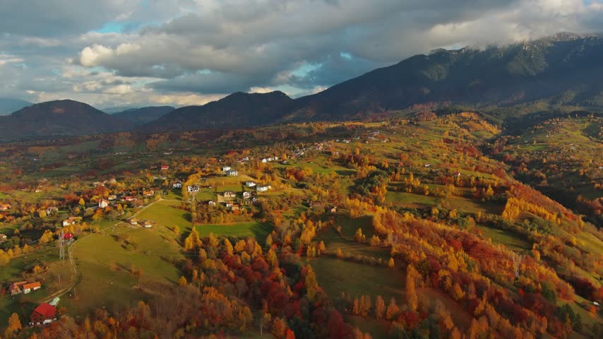 Aerial view of Transylvania landscape with colorful autumn trees, scattered houses, and rolling hills under a cloudy sky in ROMANIA.