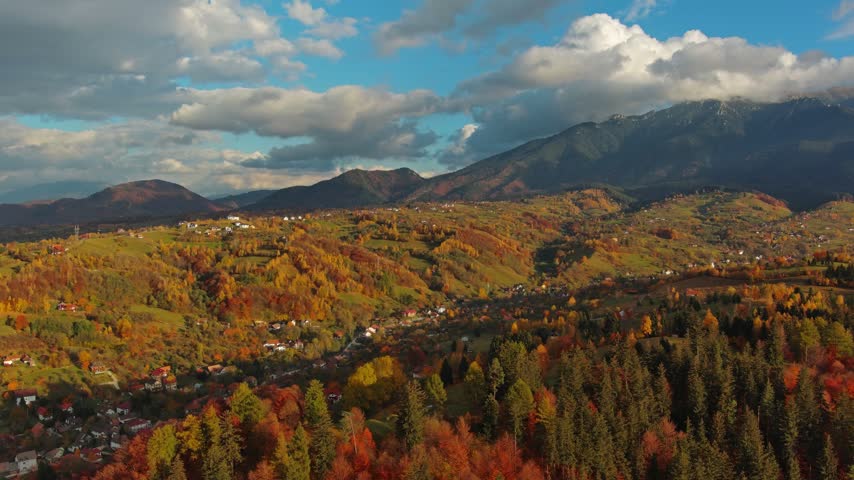 Aerial view of Transylvania landscape featuring vibrant autumn foliage, rolling hills, and dense forests under a cloudy sky in Romania.