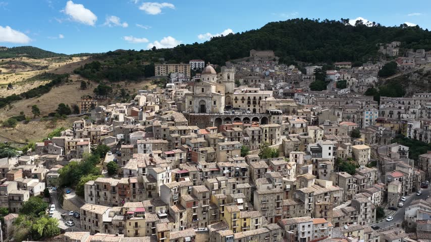 Aerial drone view of Petralia Sottana in Sicily, Italy, showing historic sicilian town buildings, churches, rooftops and traditional architecture surrounded by the Madonie mountain landscape. Sicilian hill town.