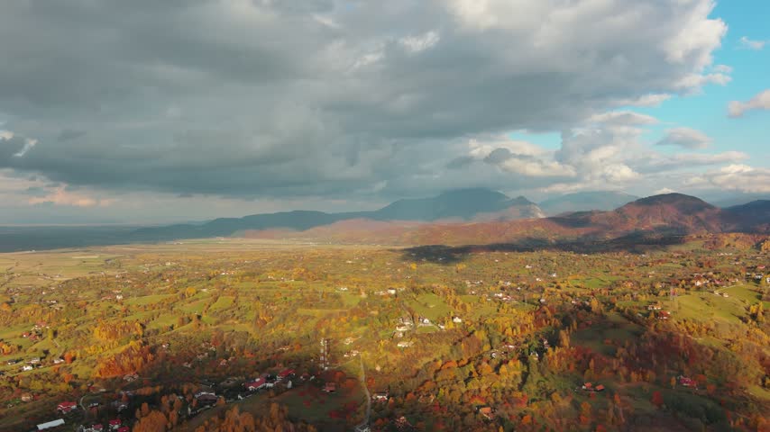 Aerial view of Transylvania landscape featuring rolling hills and mountains covered in autumn foliage under a cloudy sky in Romania.