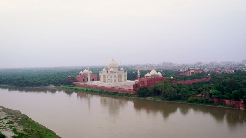 Aerial view of the Taj Mahal, a white marble mausoleum, situated on the banks of the Yamuna River, surrounded by lush gardens and historic red sandstone walls in Agra, Uttar Pradesh, India.