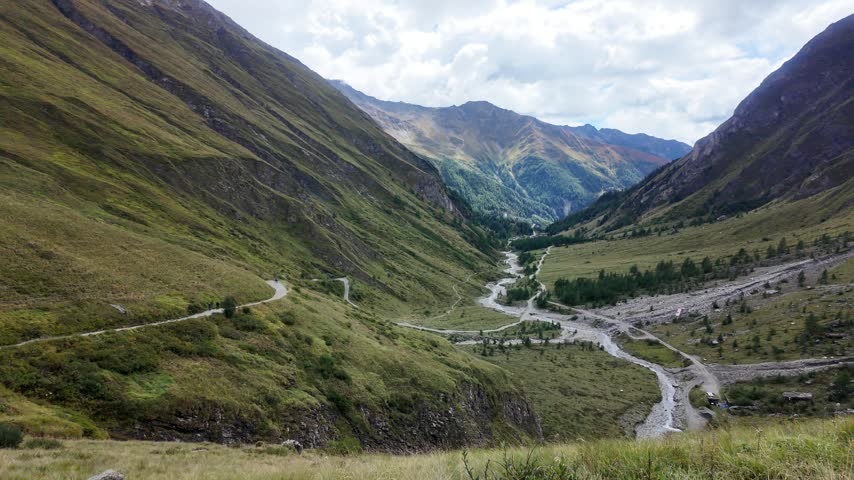 Mountain stream cascading through a rocky alpine gorge below Grossglockner, clear glacial water flowing between rugged rocks and grassy slopes in High Tauern National Park