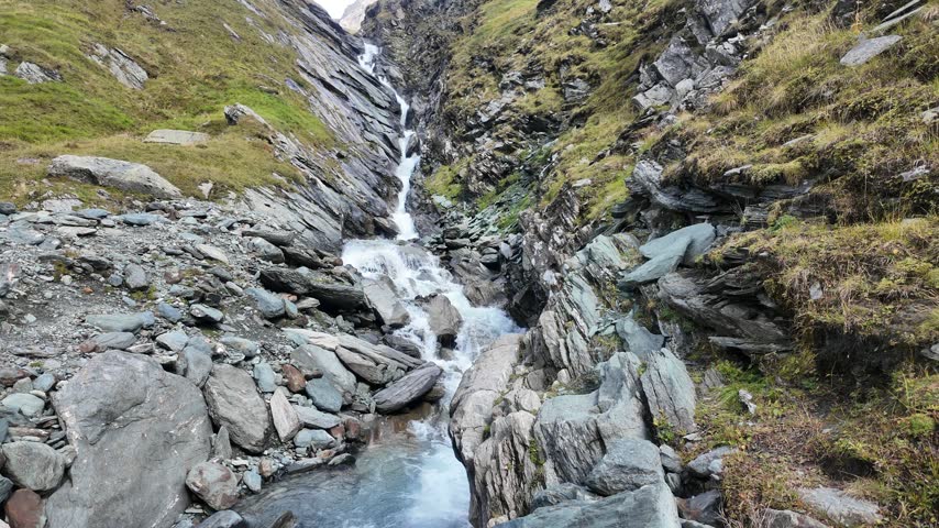 Mountain stream cascading through a rocky alpine gorge below Grossglockner, clear glacial water flowing between rugged rocks and grassy slopes in High Tauern National Park
