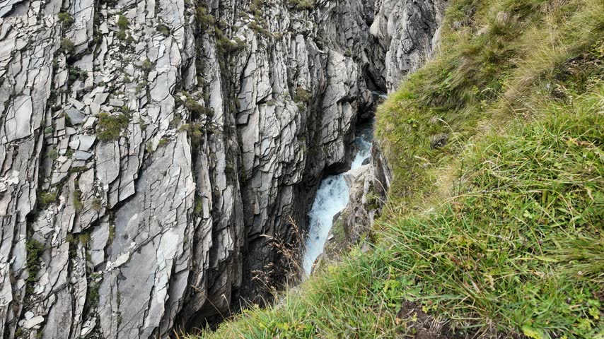 Mountain stream cascading through a rocky alpine gorge below Grossglockner, clear glacial water flowing between rugged rocks and grassy slopes in High Tauern National Park