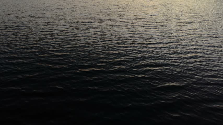 Drone advances over dark water then tilts up to reveal a Muskoka lake sunset.