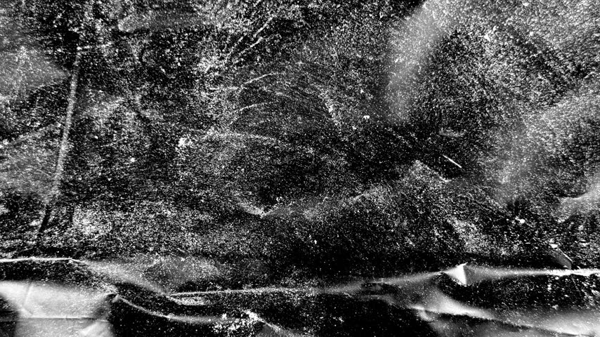 A high-contrast black and white image capturing the beauty of falling snow, with bright white flakes scattered across a deep dark background.