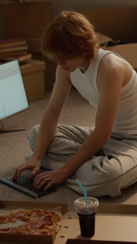 Caucasian young man sitting on floor typing on wireless keyboard. Footage suitable for student lifestyle, online education, programming courses, freelance tech marketing, vertical