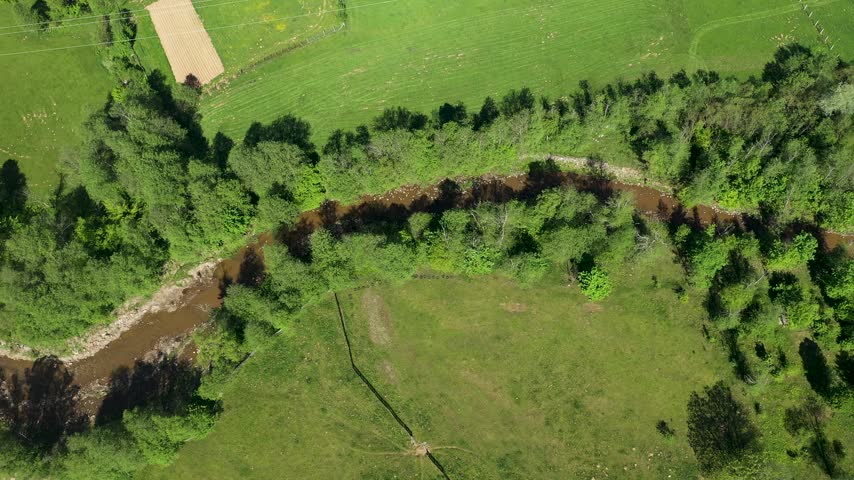 Aerial top-down view of meandering river bend and green pasture