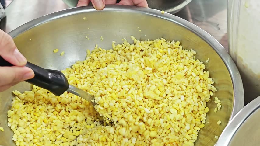 Alternative view of scooping steamed yellow split mung beans with a metal ladle.