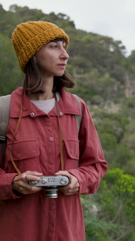 vertical shot. A woman traveler photographing mountains with an analog camera, women hold the camera and photograph nature. 
