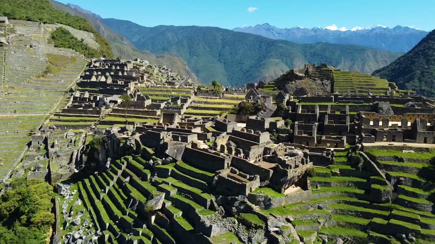 Aerial view of Historic Sanctuary of Machu Picchu featuring ancient stone ruins and agricultural terraces set against lush green mountains in Urubamba Province, Cusco, Peru.