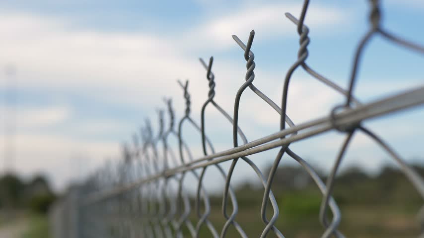 Slow motion close-up of a steel chain-link fence with twisted top wire and horizontal support rail at a rural town park oval in NSW Australia public infrastructure used for perimeter security boundary