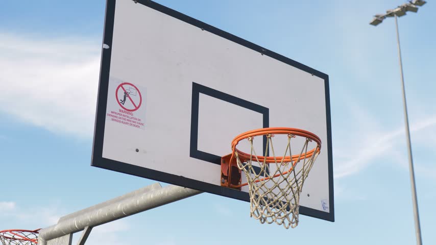 Slow motion landscape of an outdoor basketball hoop goal with a white wooden backboard net and an orange ring at a rural town suburban sports complex court facility in Australia recreation and sports
