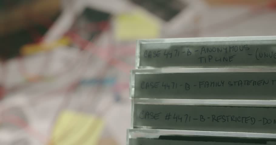 Macro pan down reveals a stack of retro cassette tapes on a detective crime desk, representing archived recordings and cold case evidence.