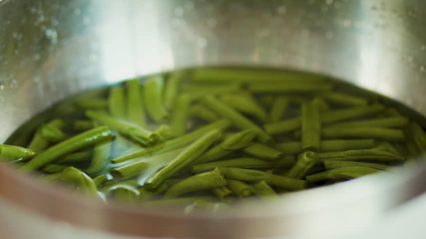 Boiled green string beans inside a metal colander bowl