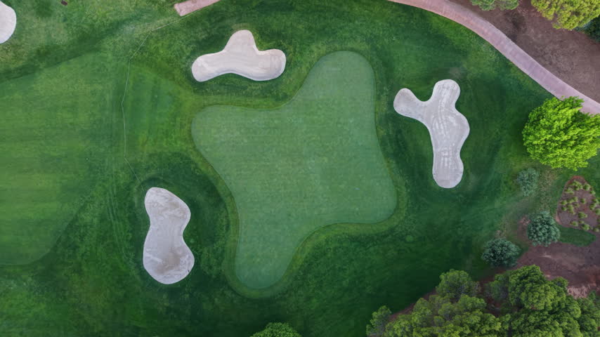 Top-down view of a golf course green surrounded by sand bunkers and lush manicured grass, with trees visible at the edges
