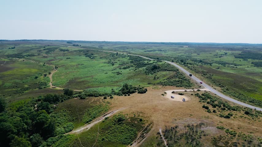 Aerial view showing open heathland with gravel car park and road cutting through green land with scattered shrubs and distant countryside nearby at Stoney Cross New Forest