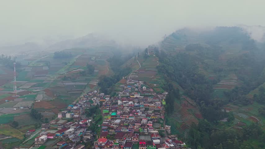 Aerial view of the colorful houses of Nepal Van Java village nestled on the misty slopes of Mount Sumbing with terraced agricultural fields in Magelang, Central Java, Indonesia.