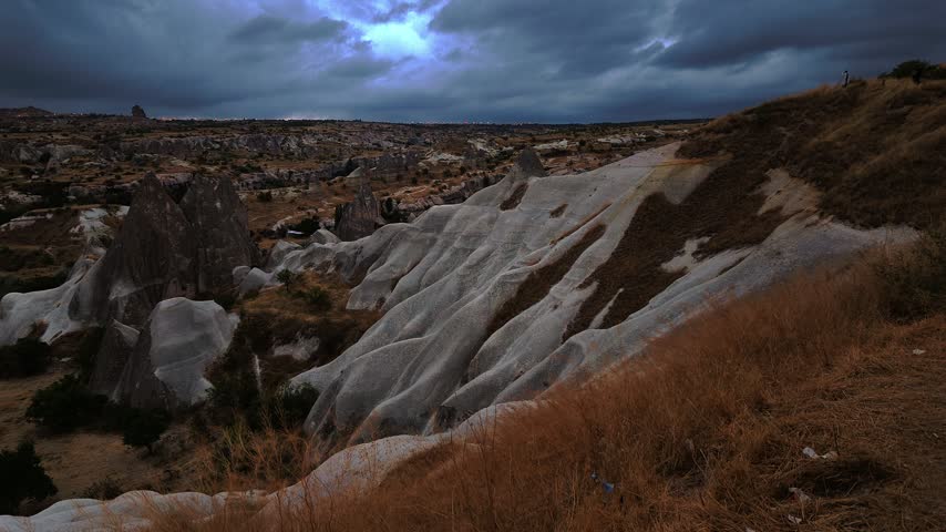 Dramatic clouds over Love Valley rock formations with dry grass foreground at dawn