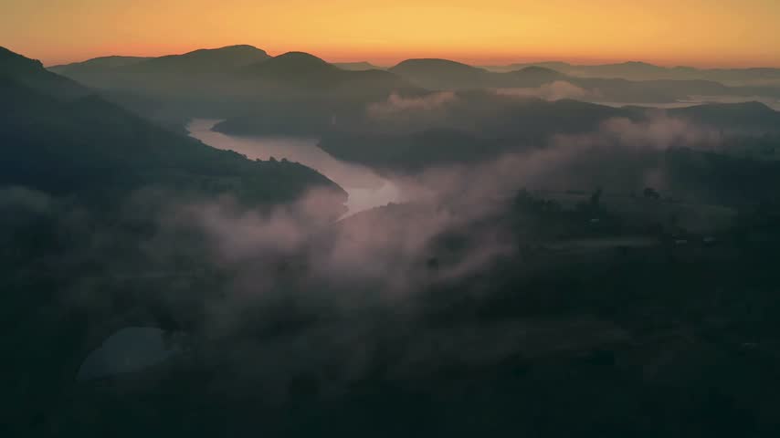 Morning light shines over hills as mist rises over a river. The landscape shows soft colors and gentle shapes. This is a natural scene with earth and water.