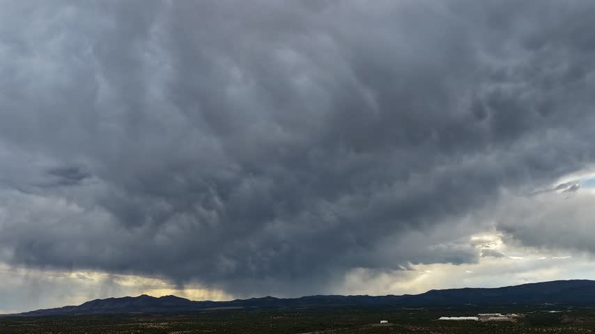 Aerial view of dark swirling storm clouds raining over the southwestern desert landscape in White Rock, NM, United States.