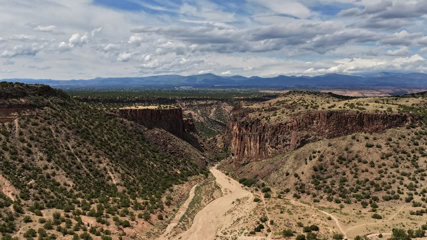 Aerial view of the rugged rock formations and desert landscape of Diablo Canyon with dramatic light and shadows under a cloudy sky in Santa Fe, New Mexico, United States.