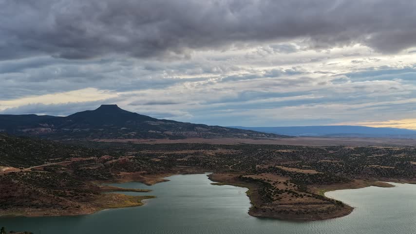 Aerial view of Pedernal Peak rising above the waters of Abiquiu Lake under a dramatic cloudy sky in Abiquiu, New Mexico, United States.