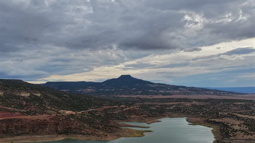 Aerial view of Pedernal Peak rising above the waters of Abiquiu Lake under a dramatic cloudy sky in Abiquiu, New Mexico, United States.