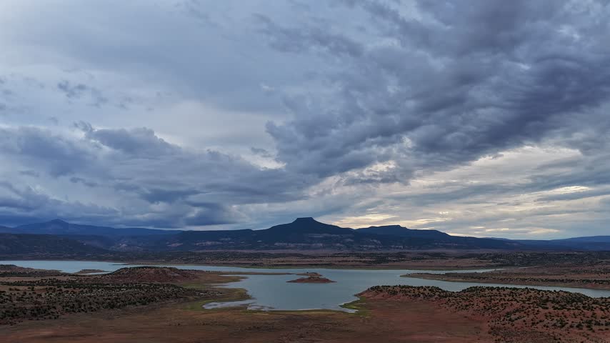 Aerial view of Pedernal Peak and Abiquiu Lake under dramatic shifting clouds in the desert landscape of Abiquiu, New Mexico, United States.