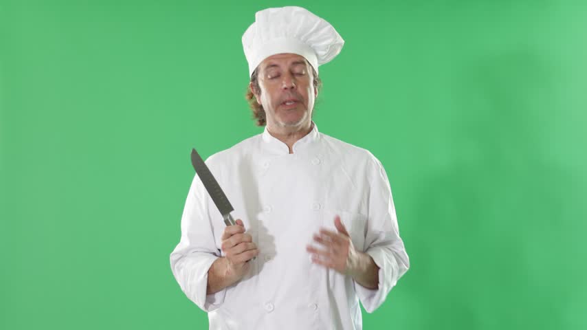 Adult male chef wearing white cook uniform and hat stands against green screen, holding chef