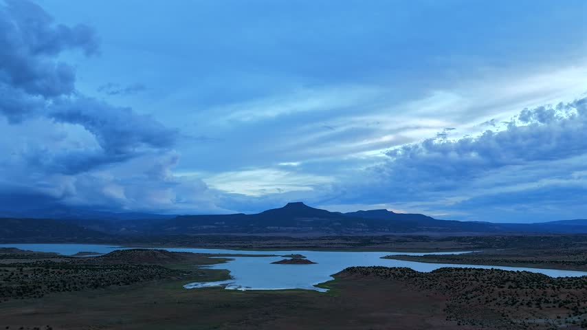 Aerial view of Cerro Pedernal rising above the waters of Abiquiu Lake during the blue hour with dramatic clouds in the sky in Abiquiu, New Mexico, United States.