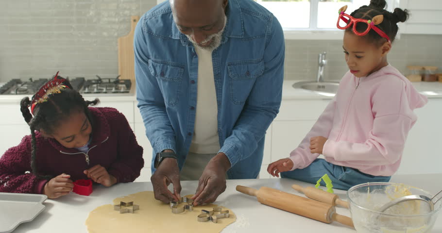 African American family baking at counter senior man guiding girls using star cutters for christmas. Kitchen, cookies, children, rolling, dough, shapes, grandparent