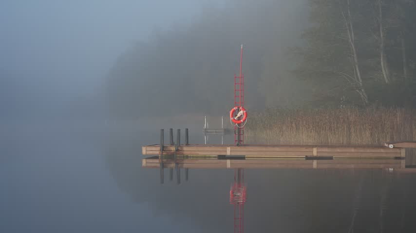 Middle aged man entering cold lake water from wooden dock early autumn morning foggy landscape Finland