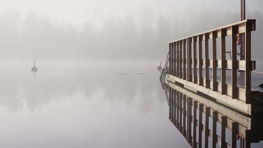 Middle aged man entering cold lake water from wooden dock early autumn morning foggy landscape Finland