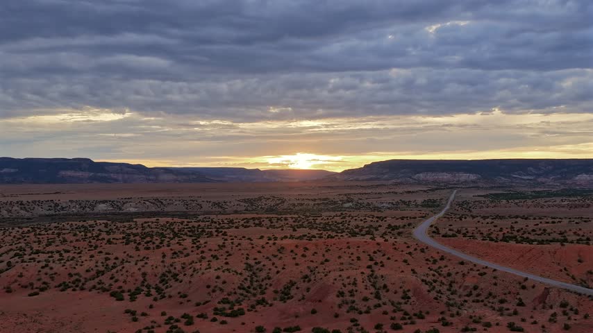 Aerial view of a highway cutting through the desert landscape of Abiquiu at sunset with dramatic clouds and mesas in Abiquiu, New Mexico, United States.