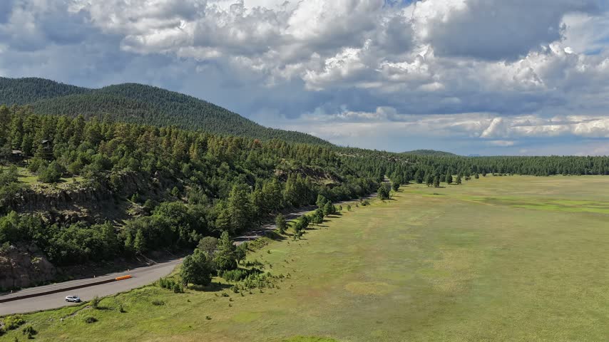 Aerial view of the Mormon Lake area featuring a scenic road, lush green meadows, and dense pine forests under a dramatic cloudy sky in Flagstaff, Arizona, United States.