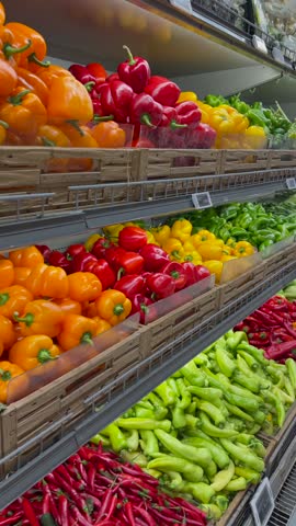 Fresh vegetables fill grocery shelves during camera movement inside supermarket aisle. Colorful bell pepper selections, zucchini and green beans present abundant healthy food retail options.