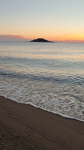 Breathtaking views of the sunset reflecting on the calm waters of Sardinia, Italy. The serene scene captures gentle waves lapping at the sandy beach, creating a peaceful atmosphere.